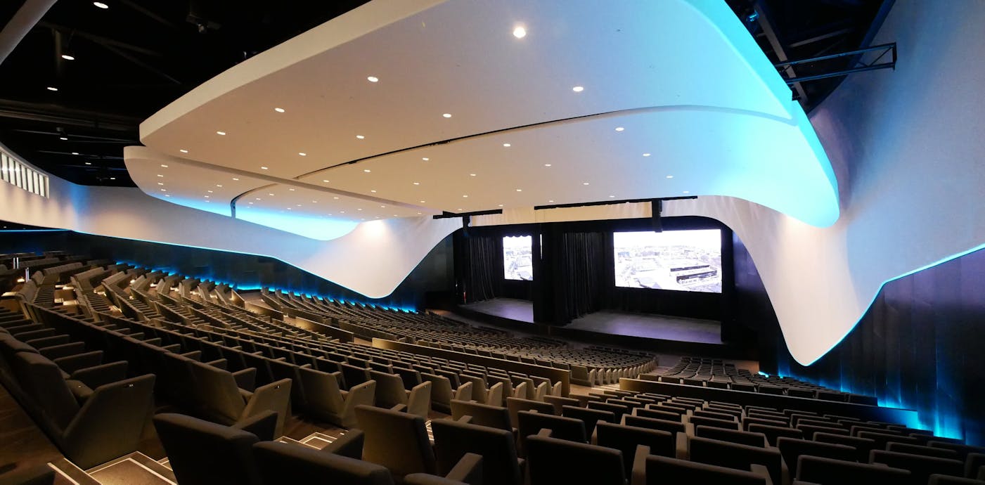 A modern auditorium features tiered seating and a sleek, curved ceiling with blue lighting. The stage is set for performances, allowing for engaging events under the Te Pae brand.
